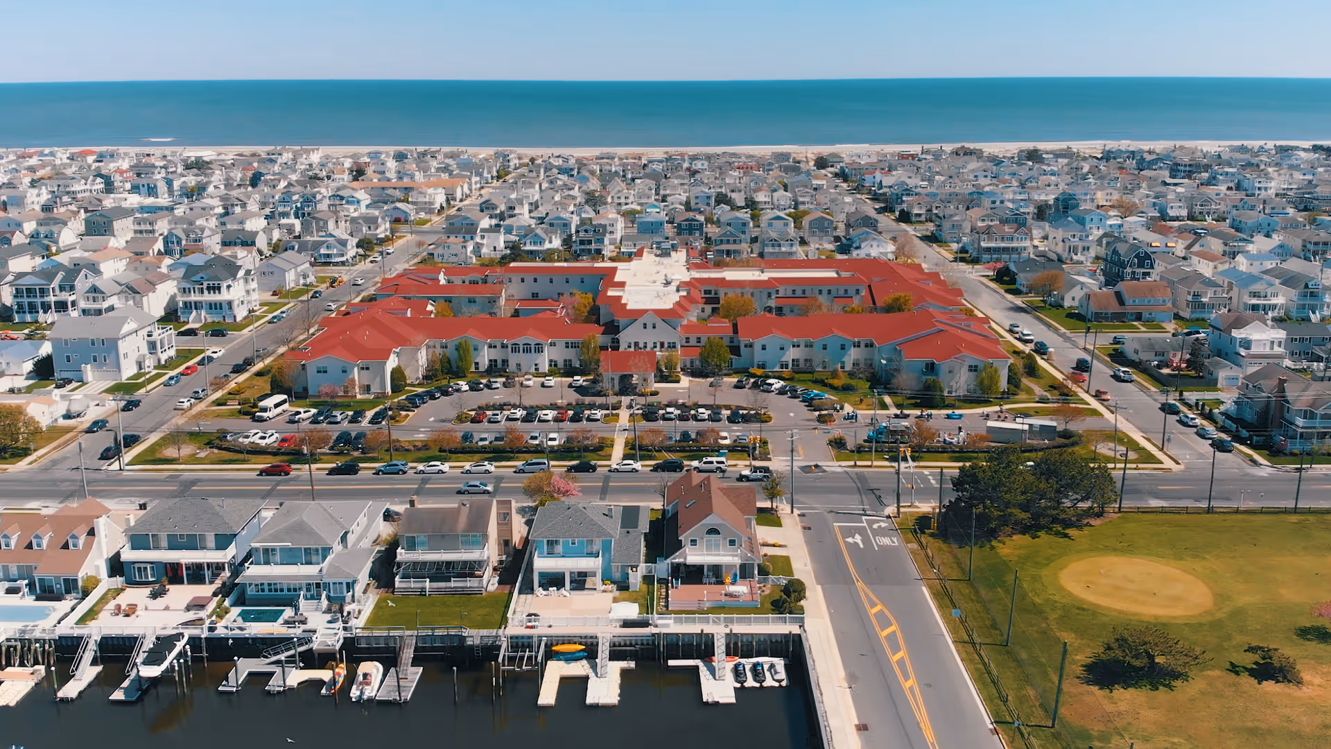 Aerial view of a coastal senior living campus with red-roofed buildings near the shore.