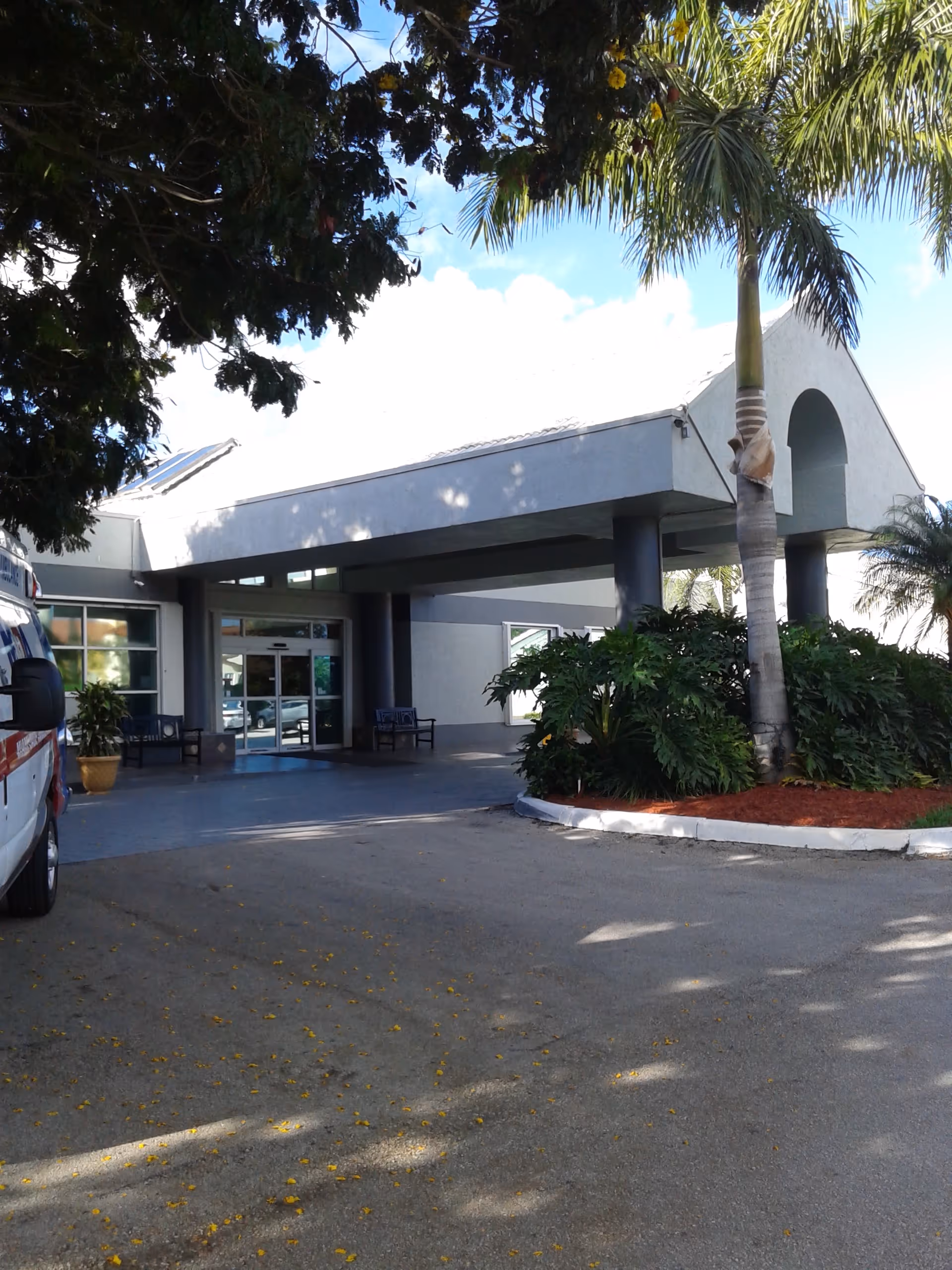 Exterior view of Coral Reef Subacute Care Center entrance with palms and parked vehicle.