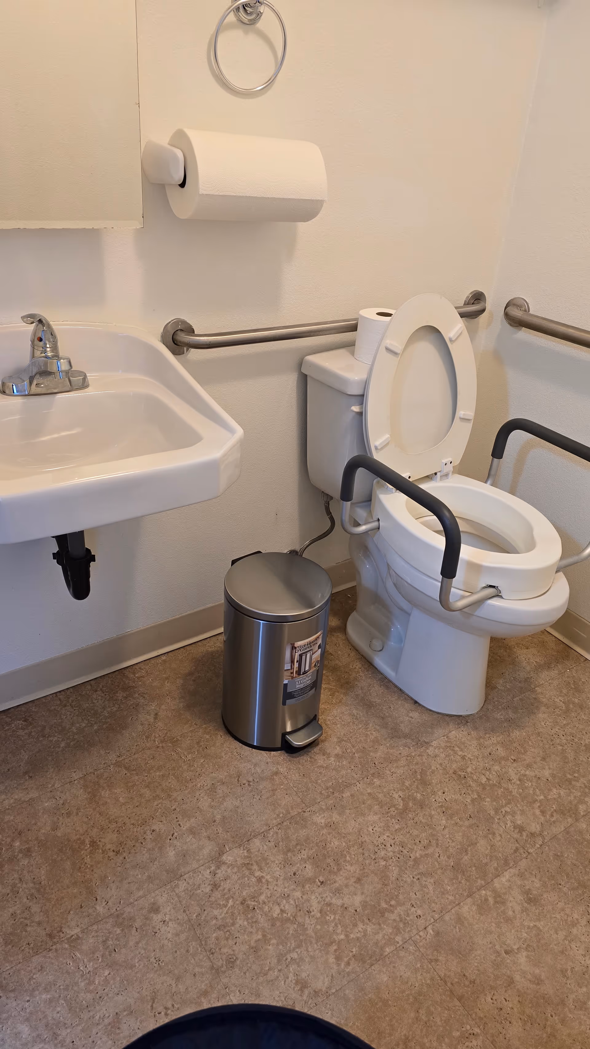 Accessible restroom with sink, toilet, grab bars, and trash can in a care facility.