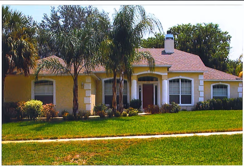 Front view of a single-story yellow senior living building with palm trees and a green lawn