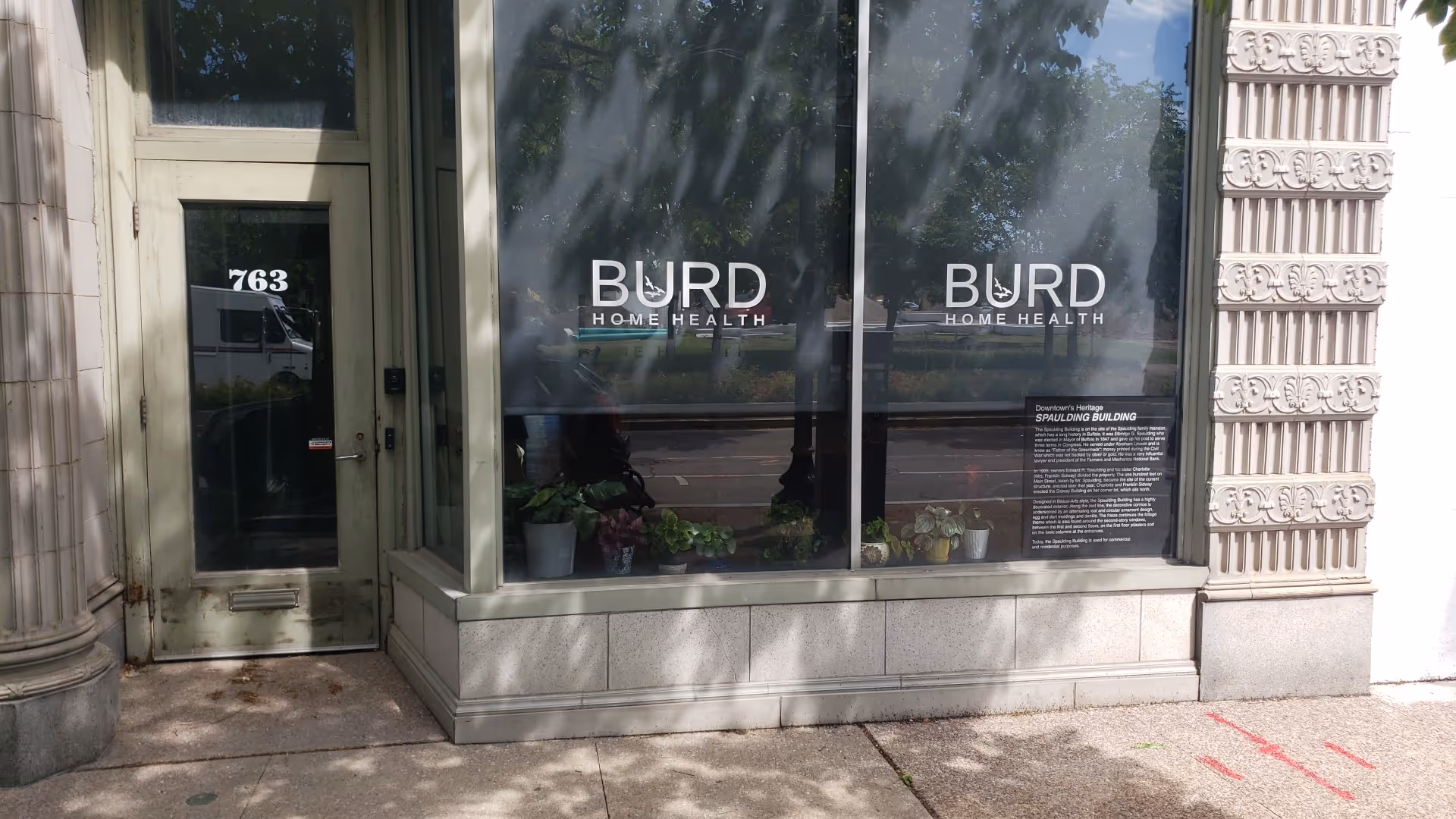 Front window of Burd Home Health with plants and a left door.