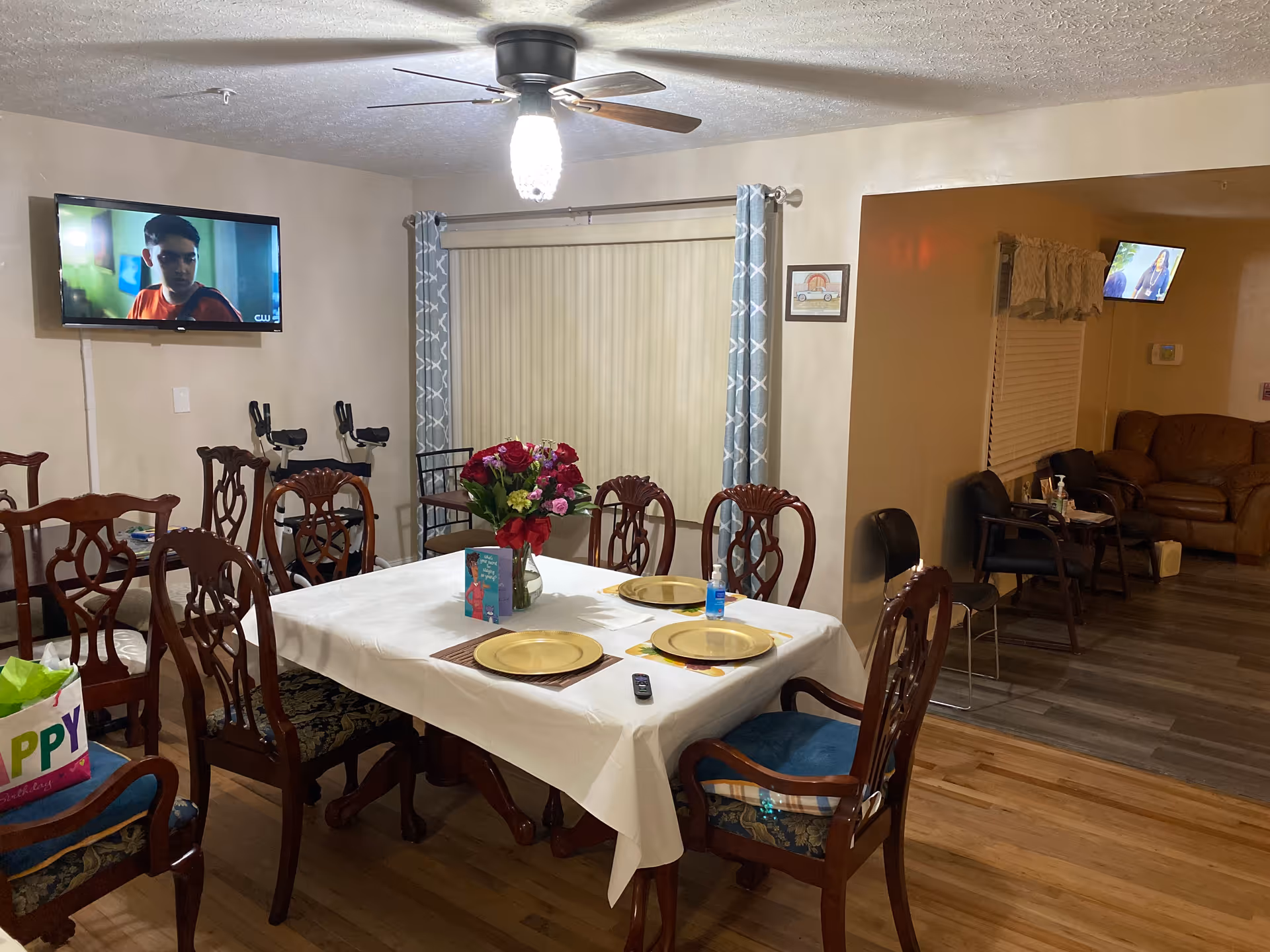 Communal dining room with a table set for a meal, floral centerpiece, and a wall TV.