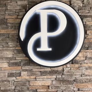 Circular illuminated logo sign mounted on a stone building facade.