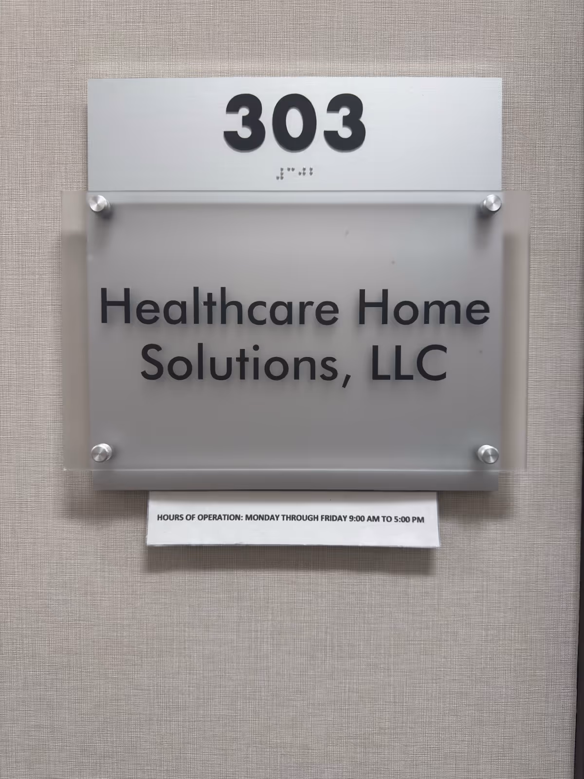A frosted glass sign with Healthcare Home Solutions, LLC, room 303, and hours on a wall.