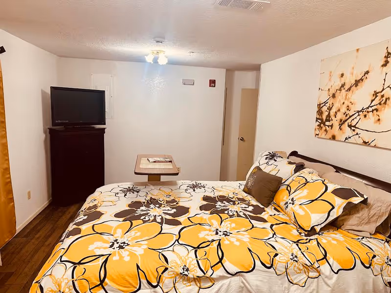 A cozy bedroom in Rosewood Assisted Living with a floral bedspread, TV, and wall art.