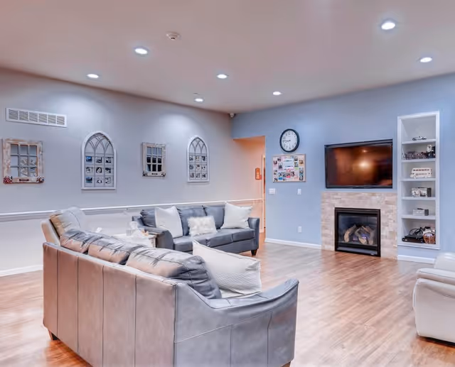 Northport Apartments' communal living room with gray leather sofas, fireplace, TV, and shelves.