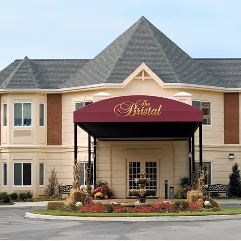 Exterior view of The Bristal Assisted Living at Massapequa with entrance canopy and fountain.