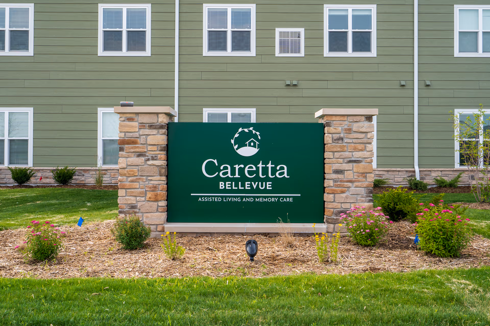 Green Caretta Bellevue sign with stone pillars in front of a multi-story building.