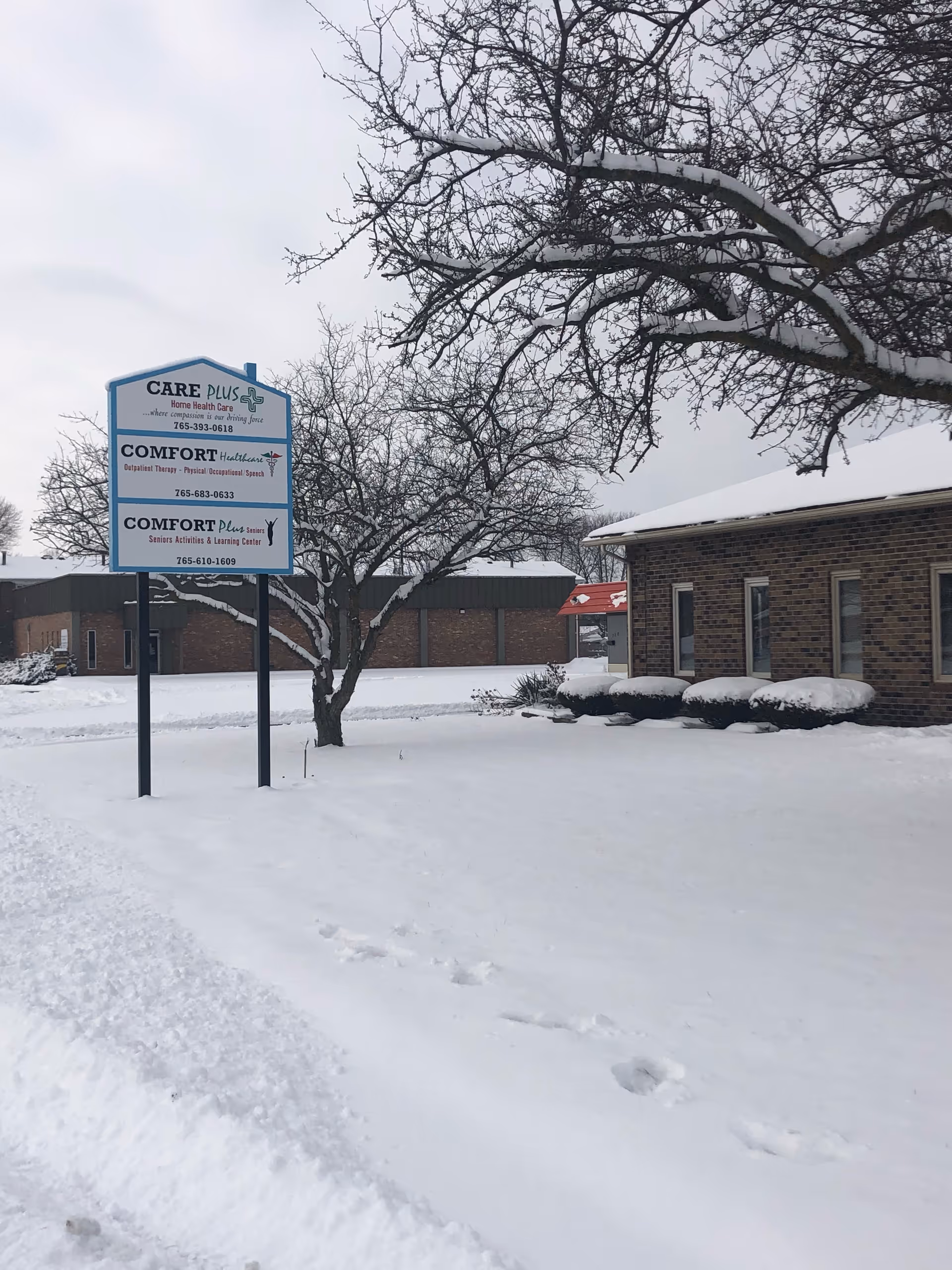 Snowy exterior view with Care Plus Home Health Care sign beside a brick building