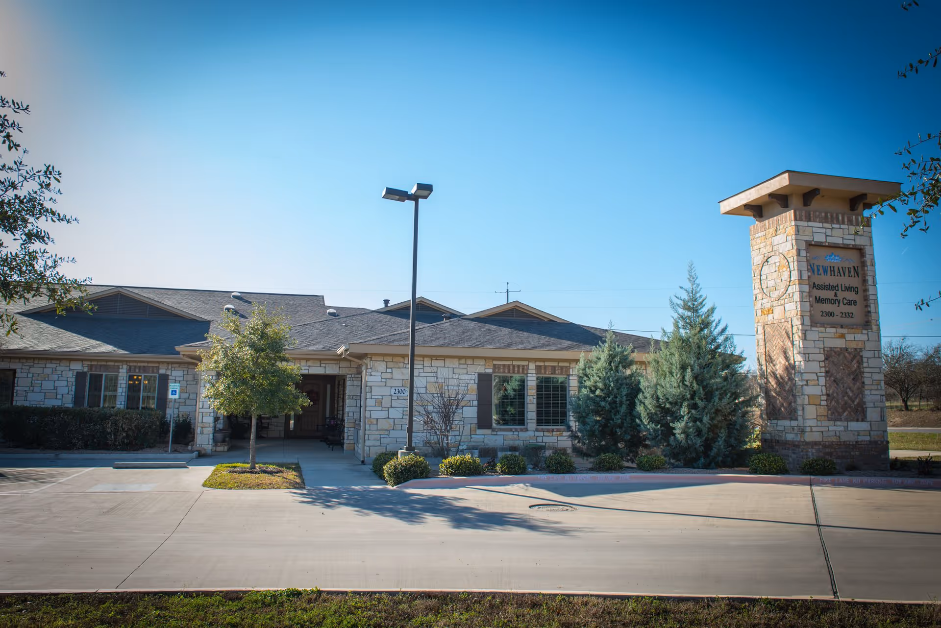Exterior view of New Haven Assisted Living building with stone facade, sign tower, and landscaping.