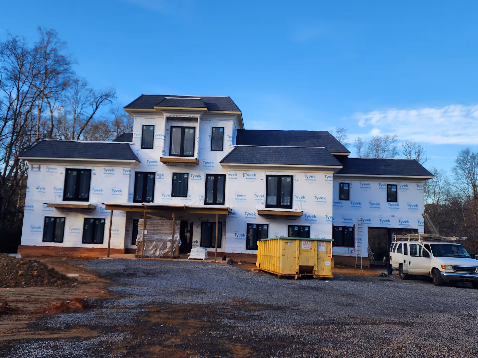 A large house-style building under construction with Tyvek wrap and construction equipment.