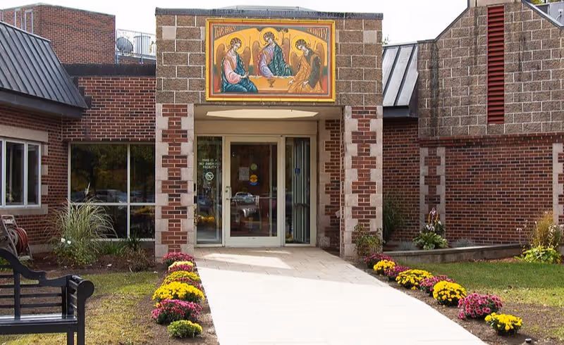 Front entrance of Holy Trinity Nursing and Rehabilitation Center with brick facade and flower beds.