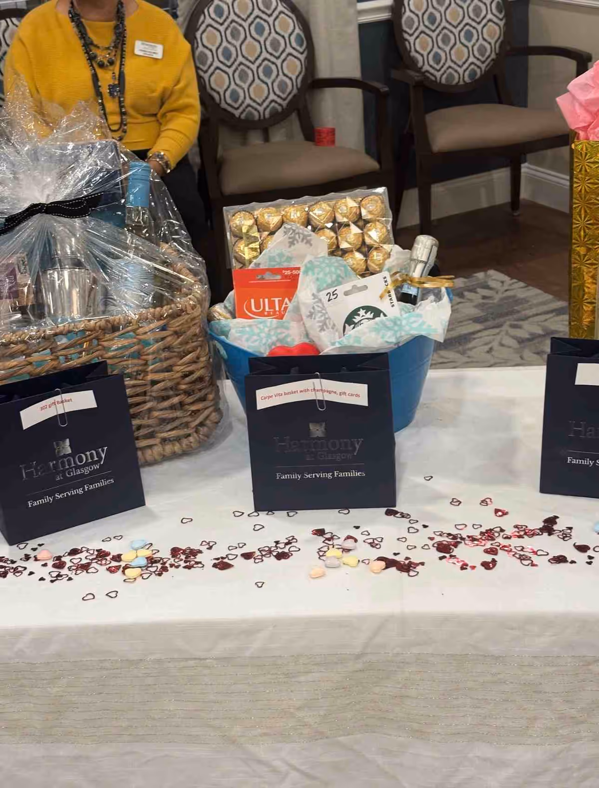 Indoor gift display on a table with baskets, bags, and scattered hearts at a care event.