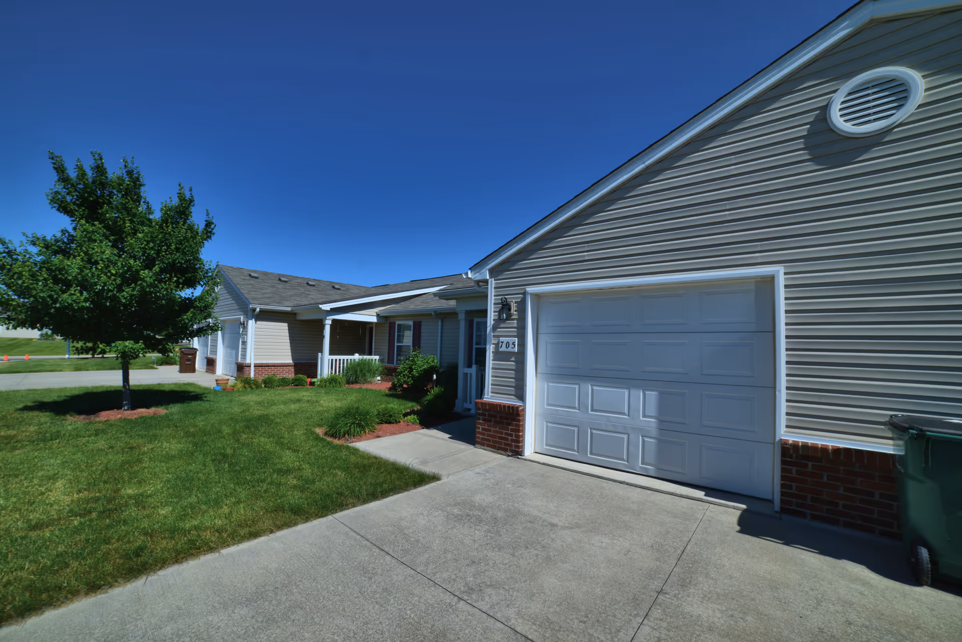 Front exterior of a single-story senior living villa with driveway and lawn.