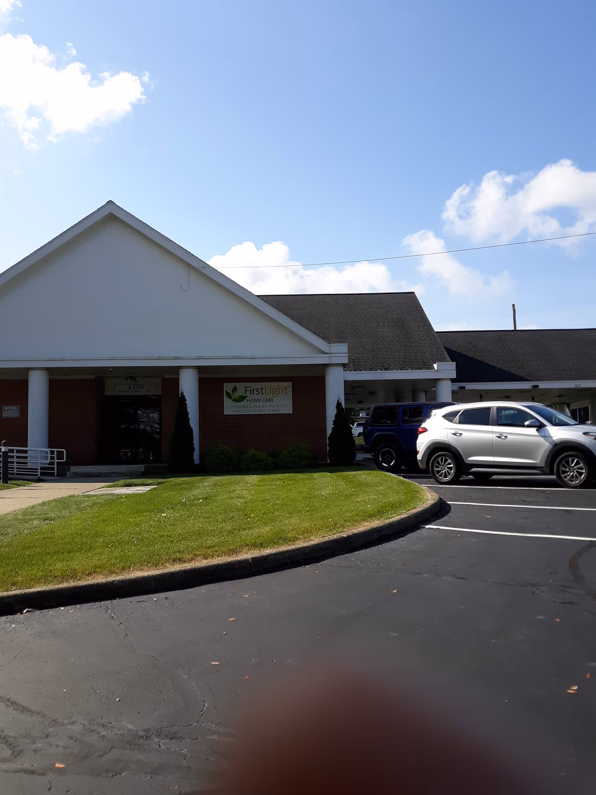 Exterior view of FirstLight Home Care facility with entrance, sign, and parked cars.