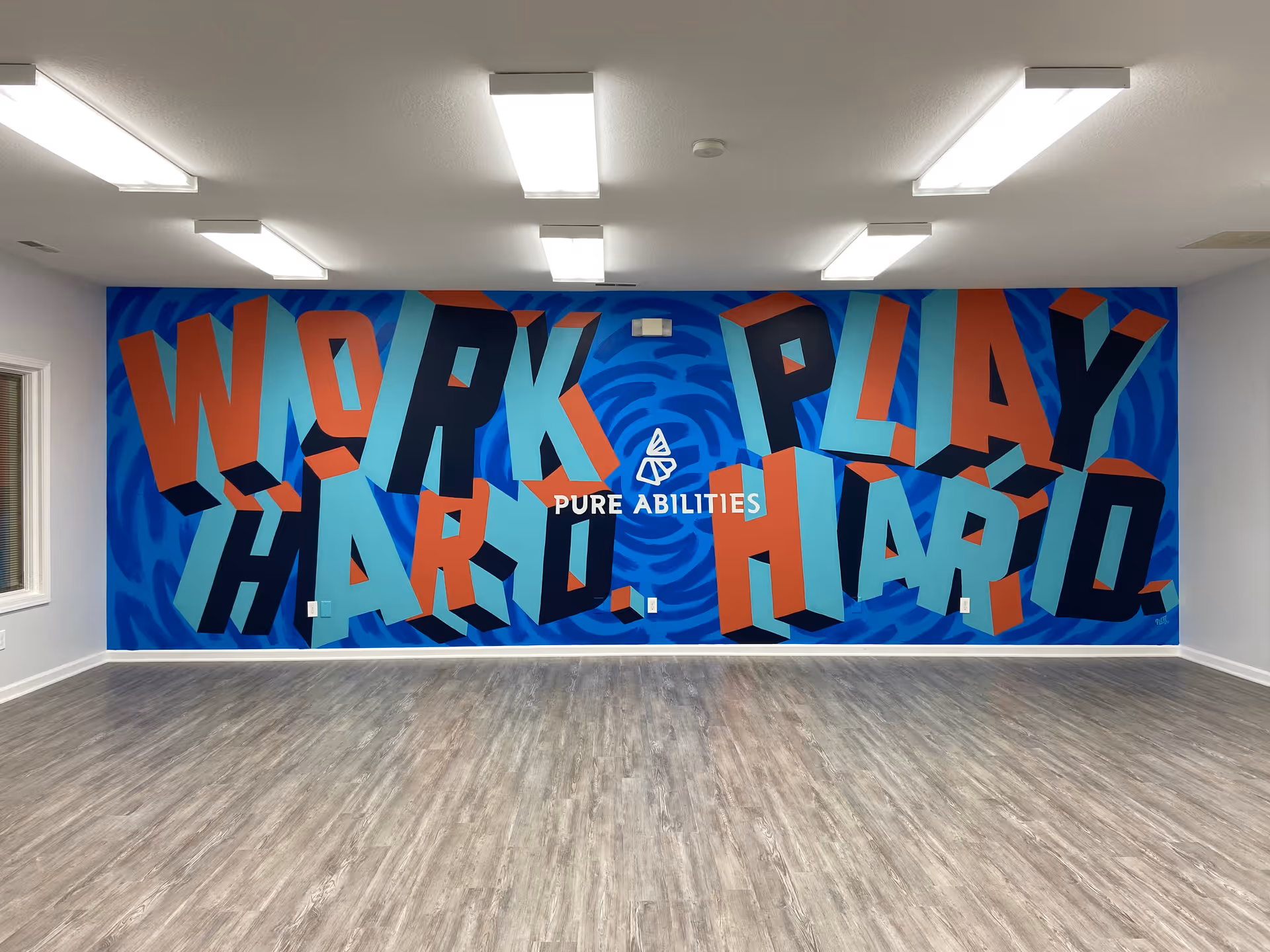 Interior room with a bold blue mural saying 'WORK PLAY HARD' and 'PURE ABILITIES'.