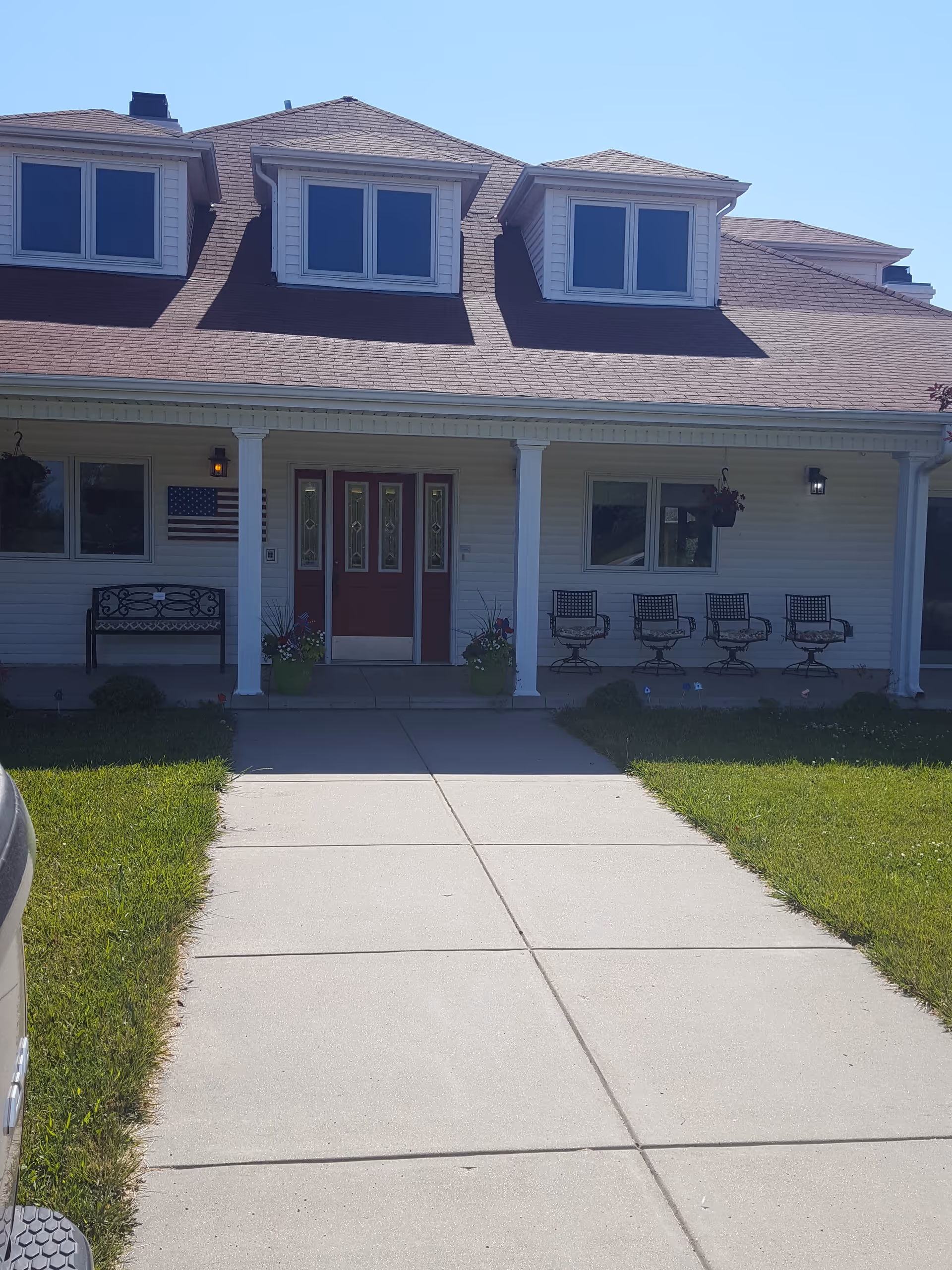 Front entrance of a white senior living building with porch chairs.