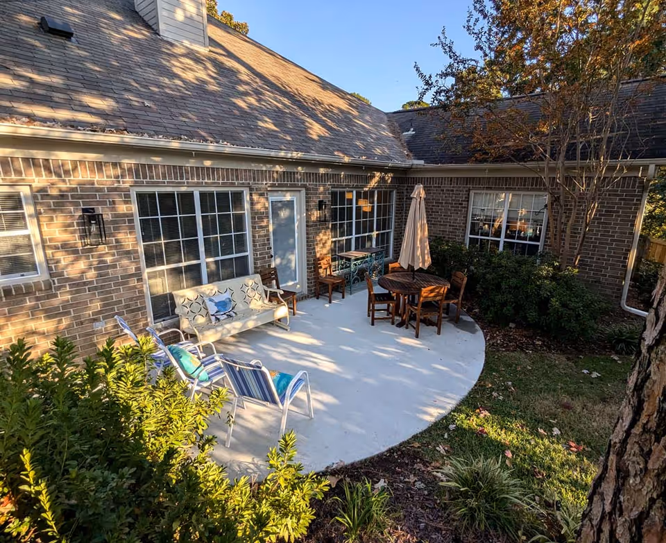 Brick home exterior with curved concrete patio, outdoor furniture, and a table under an umbrella.