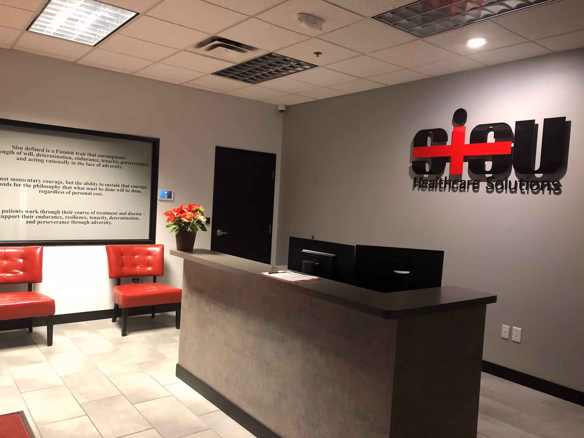 Reception area with curved counter, computers, red chairs, plant, and Sisu Healthcare Solutions logo.