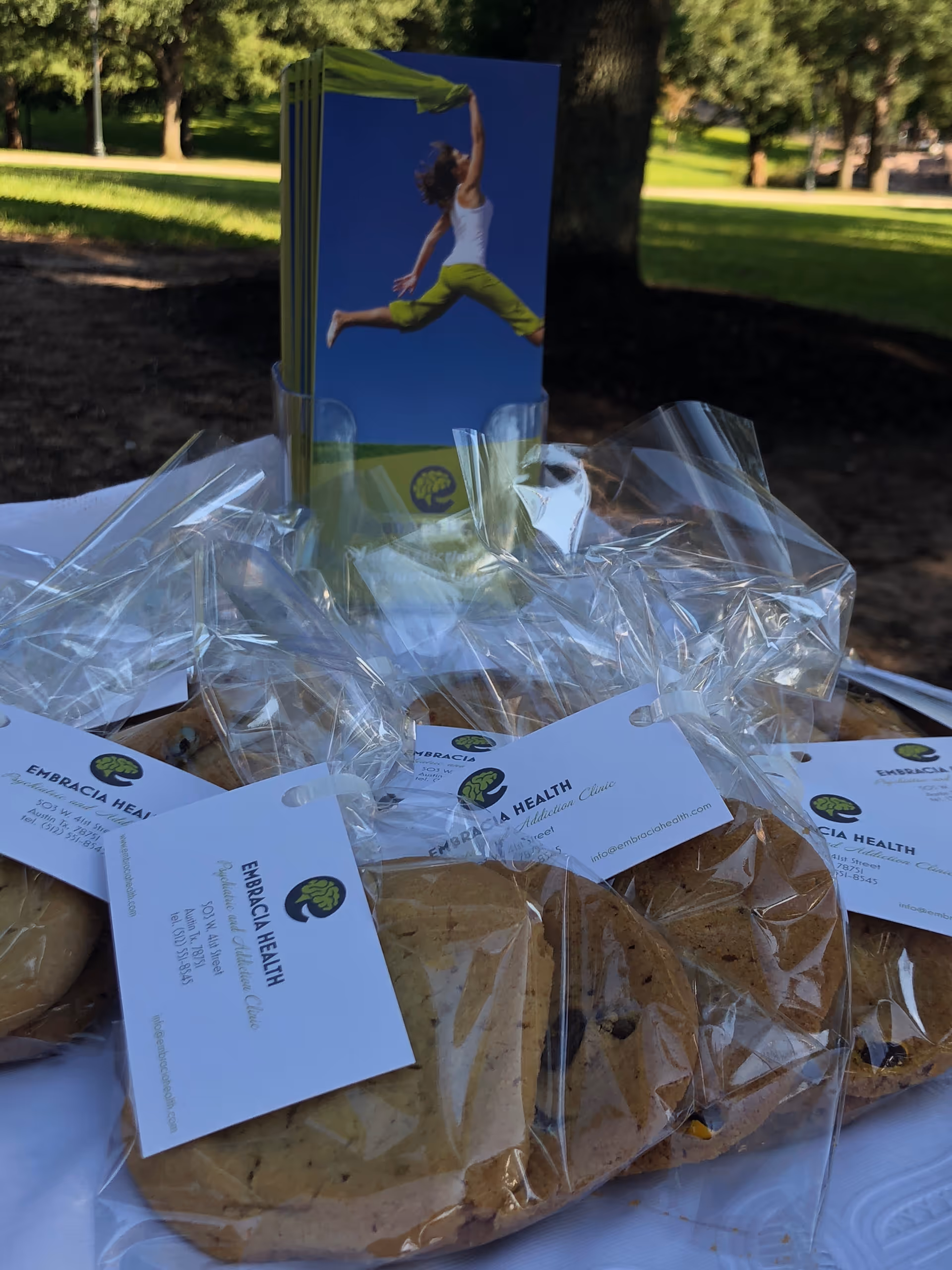 Outdoor table with wrapped pastries and Embracia Health cards in a park setting.