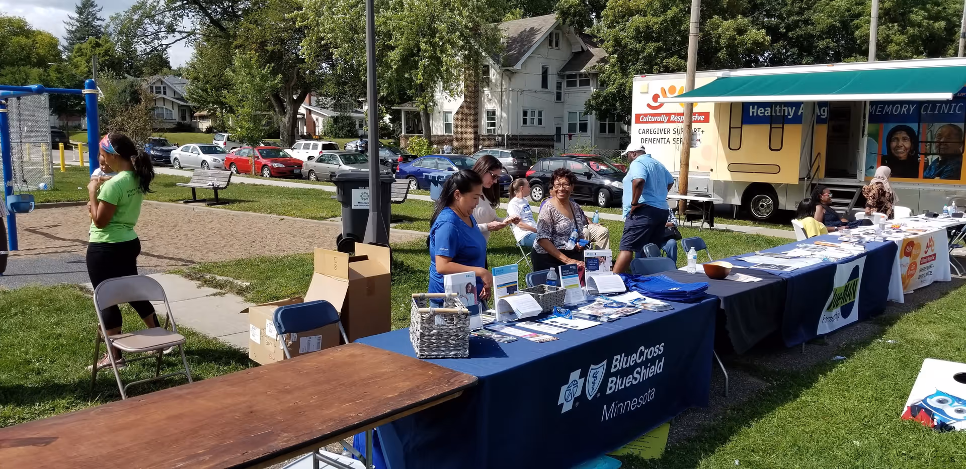 Outdoor health fair with multiple information booths and attendees gathered around tables.