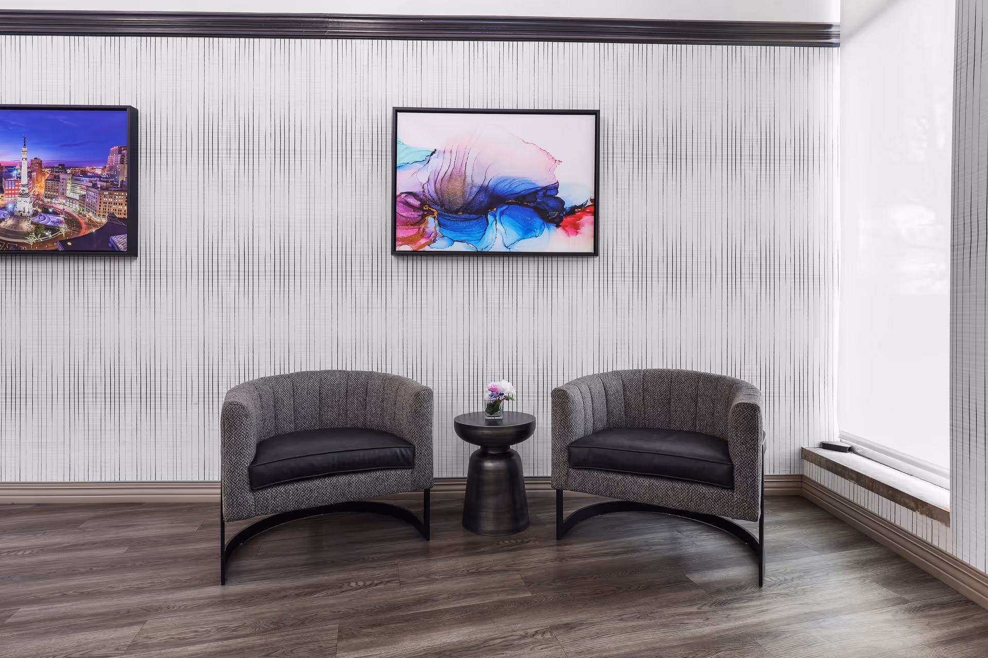 Two curved gray chairs face a small round table with a flower in a contemporary lobby.