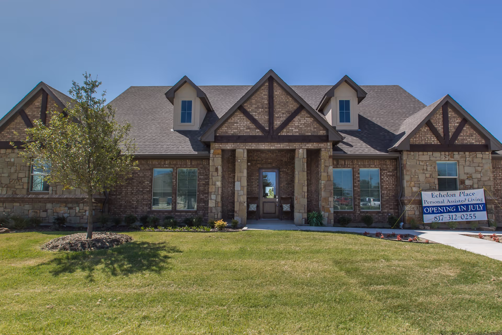 Front exterior of the Echelon Place assisted living building with a lawn and a sign announcing an opening in July.