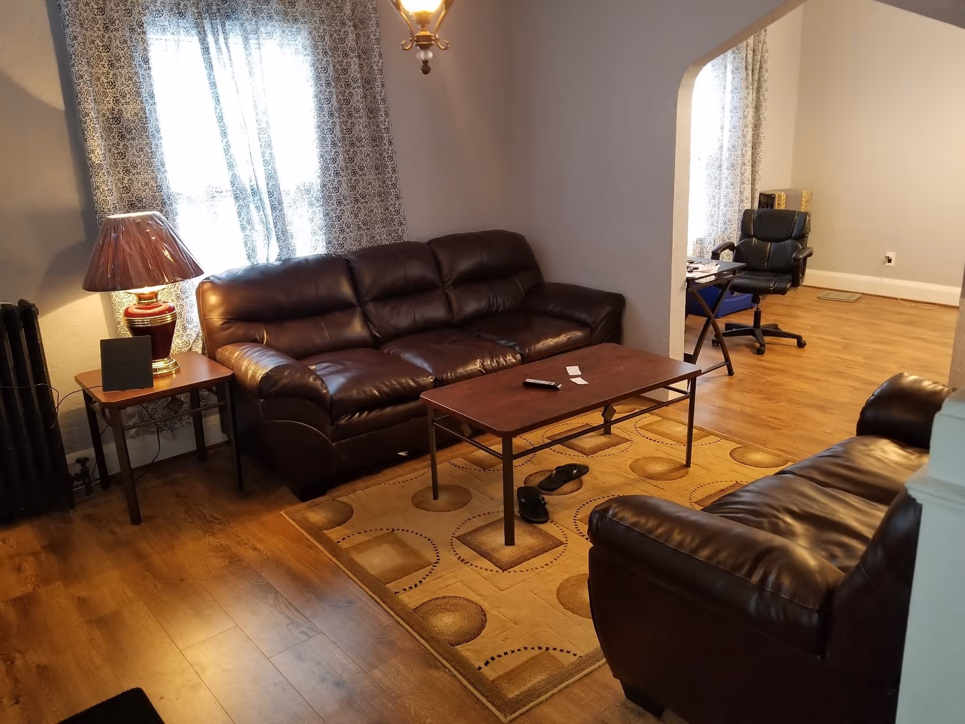 Cozy living room with leather sofas, coffee table, rug, and an office area in back.