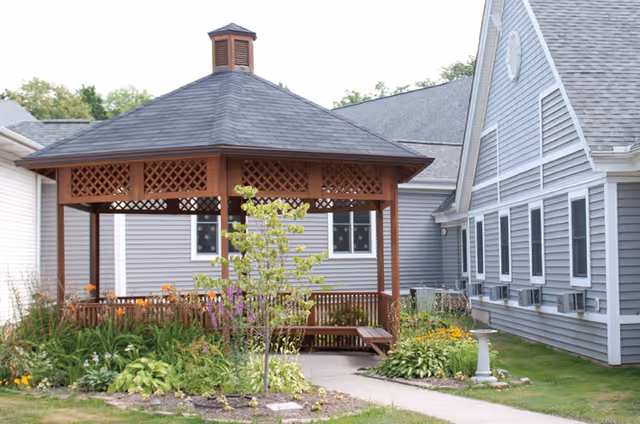 A wooden gazebo in a landscaped outdoor courtyard beside a light gray senior living building.