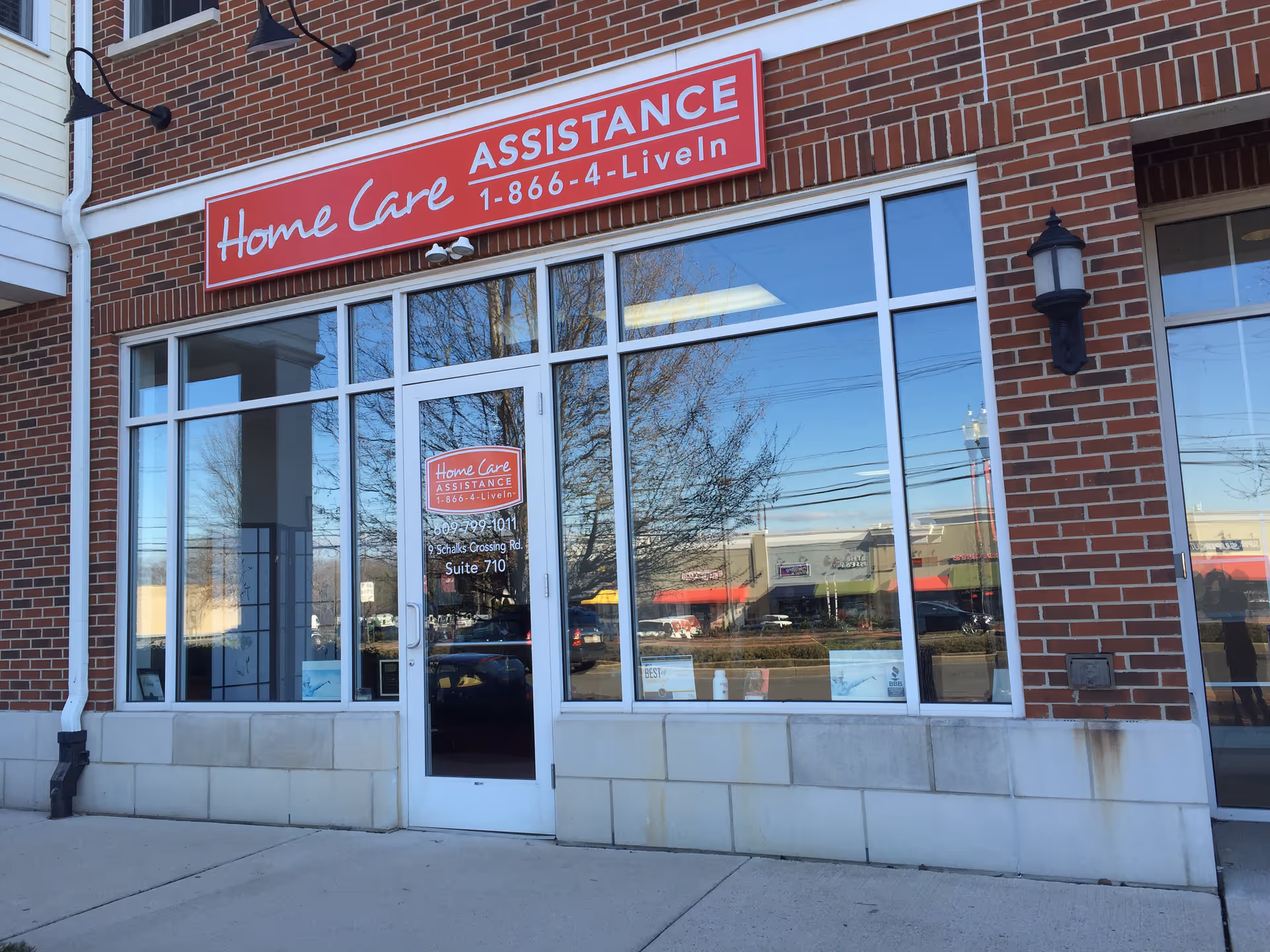 Brick storefront with large glass windows and a red Home Care Assistance sign