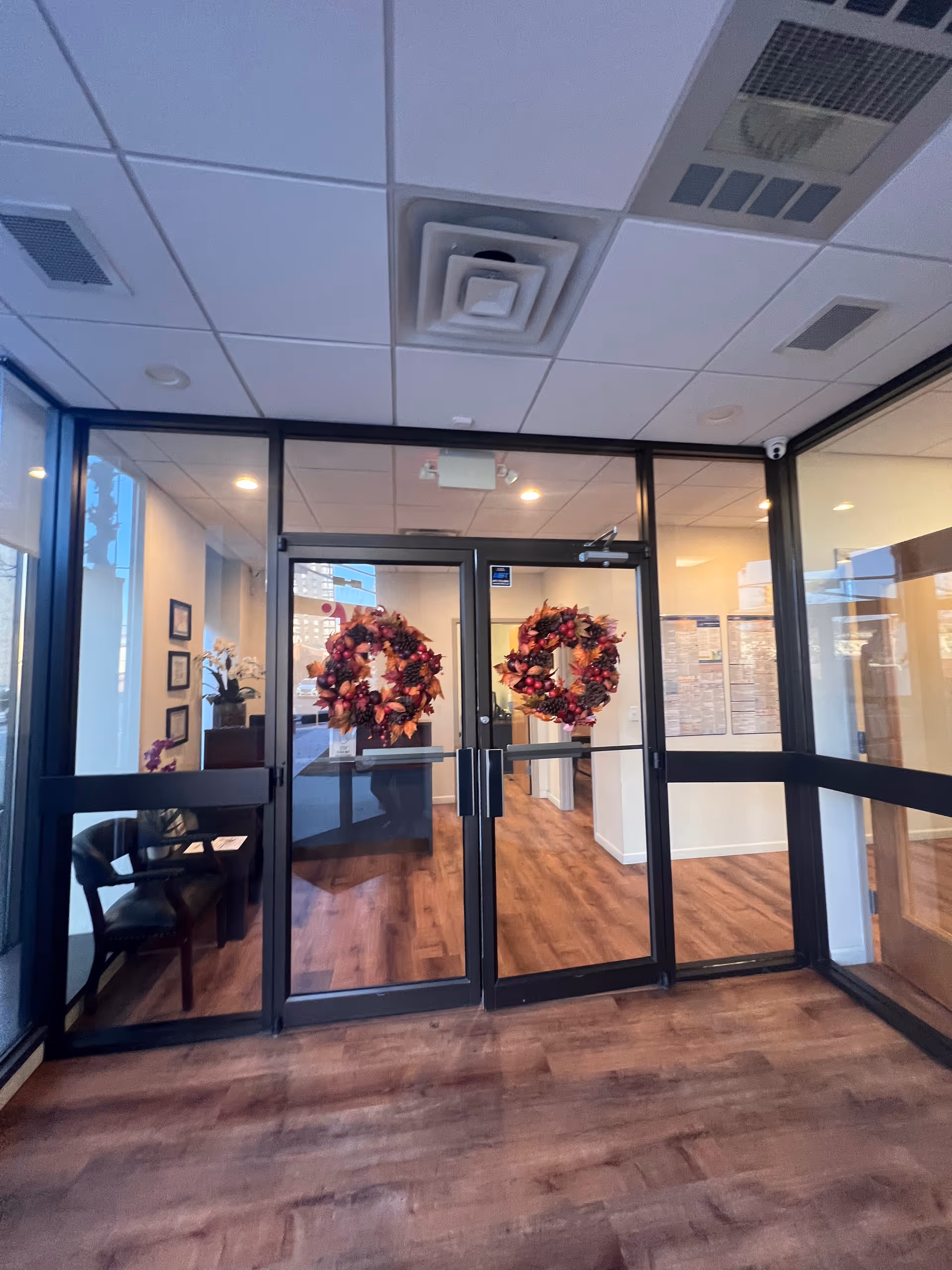 Glass front doors of a senior living lobby with holiday wreaths and wood flooring.