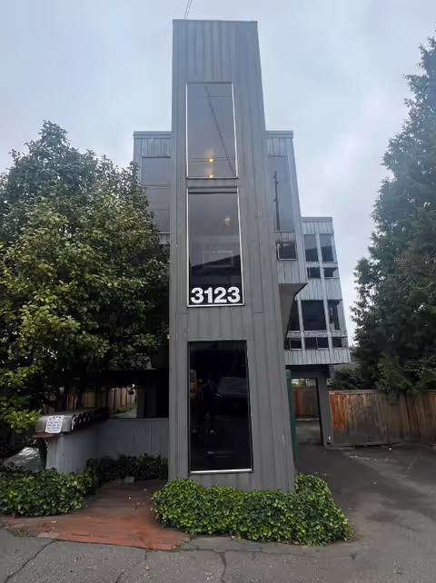 Tall gray modern building with large windows and the number 3123 on its front facade.