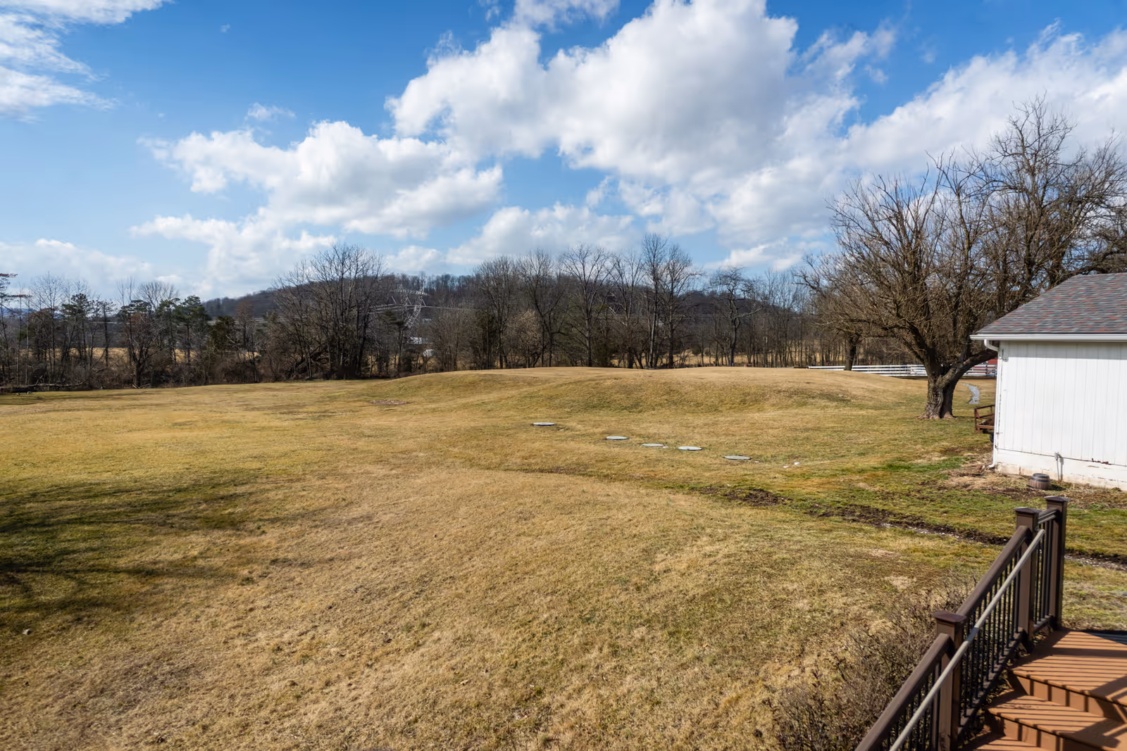 Spacious grassy outdoor area with a white building, bare trees, and a wooden railing.