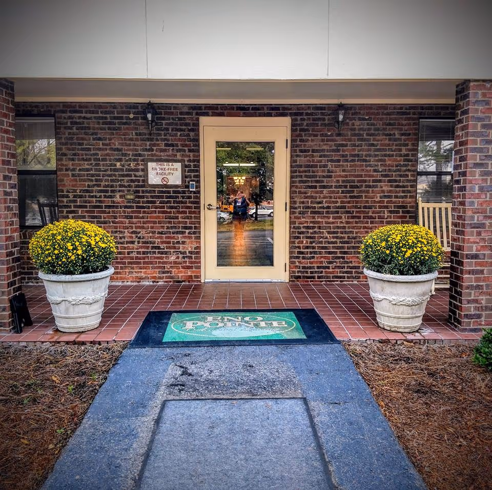 Entrance of Eno Pointe Assisted Living with potted plants and a welcome mat.