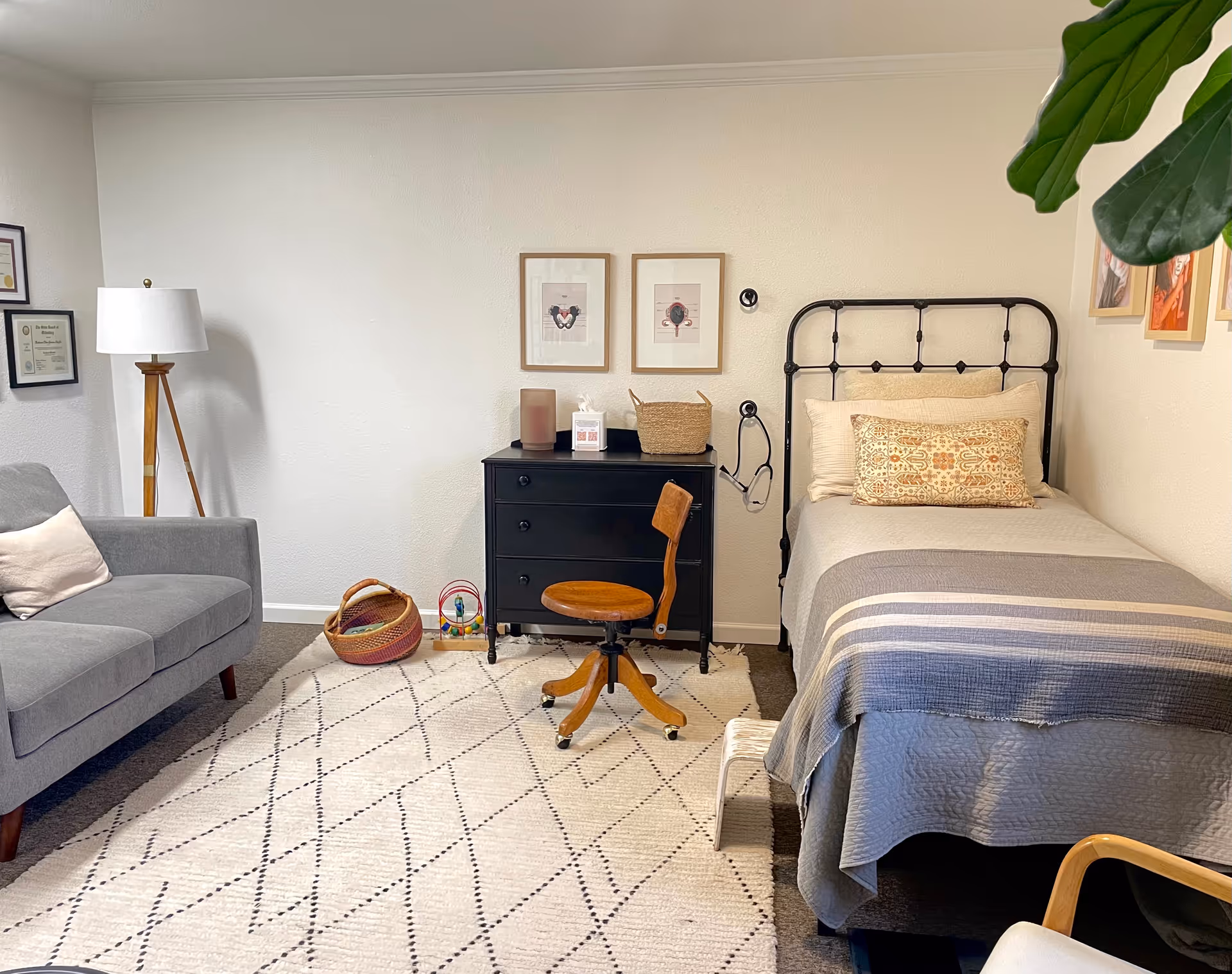 Cozy bedroom with a metal-framed bed, black dresser, chair, sofa, lamp, and patterned rug.