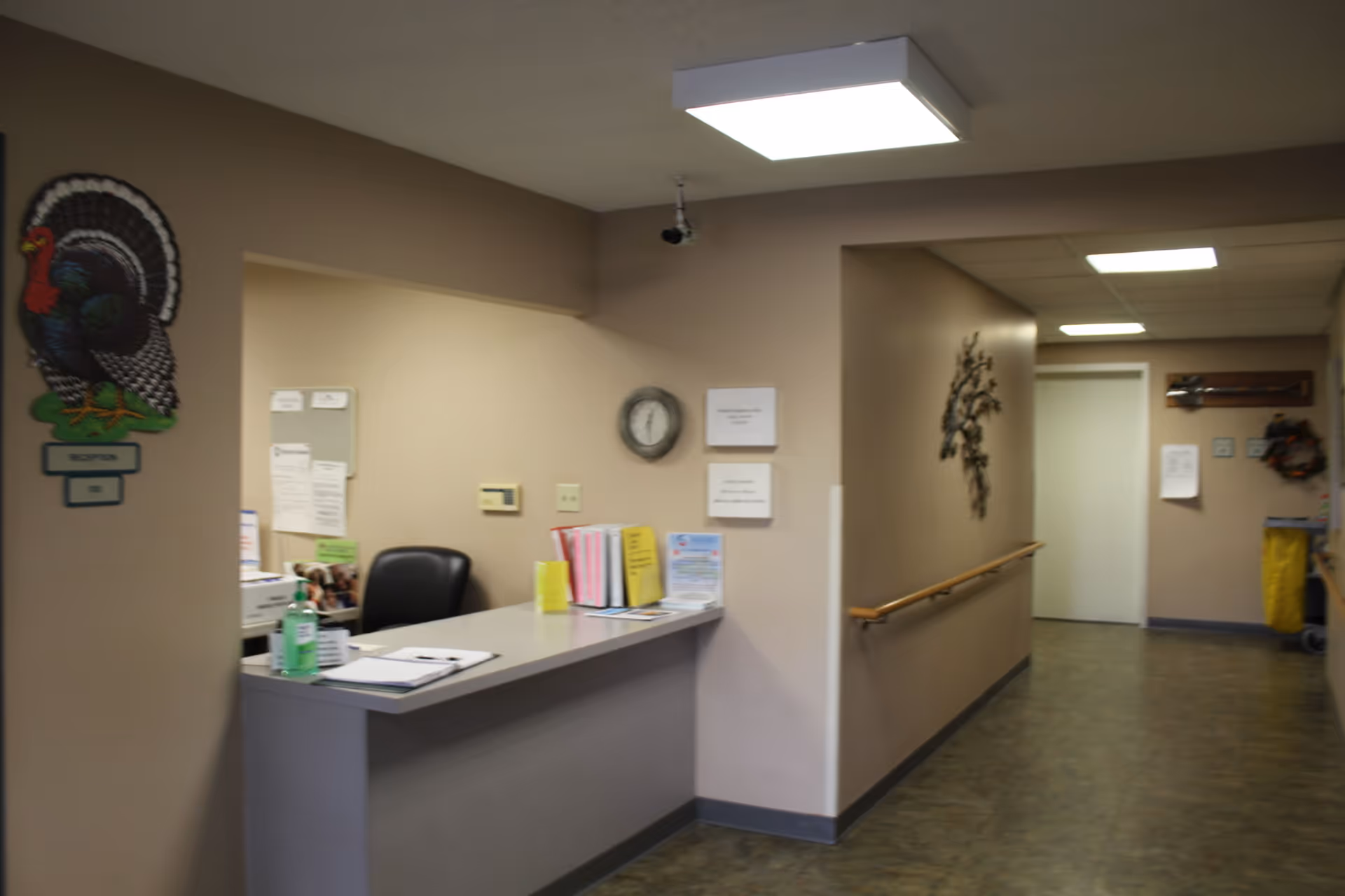 Interior hallway with a reception desk, bulletin boards, clock, and a mural turkey near entrance.