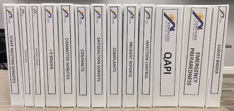 Row of white binders labeled satisfaction surveys and other documents on a shelf.