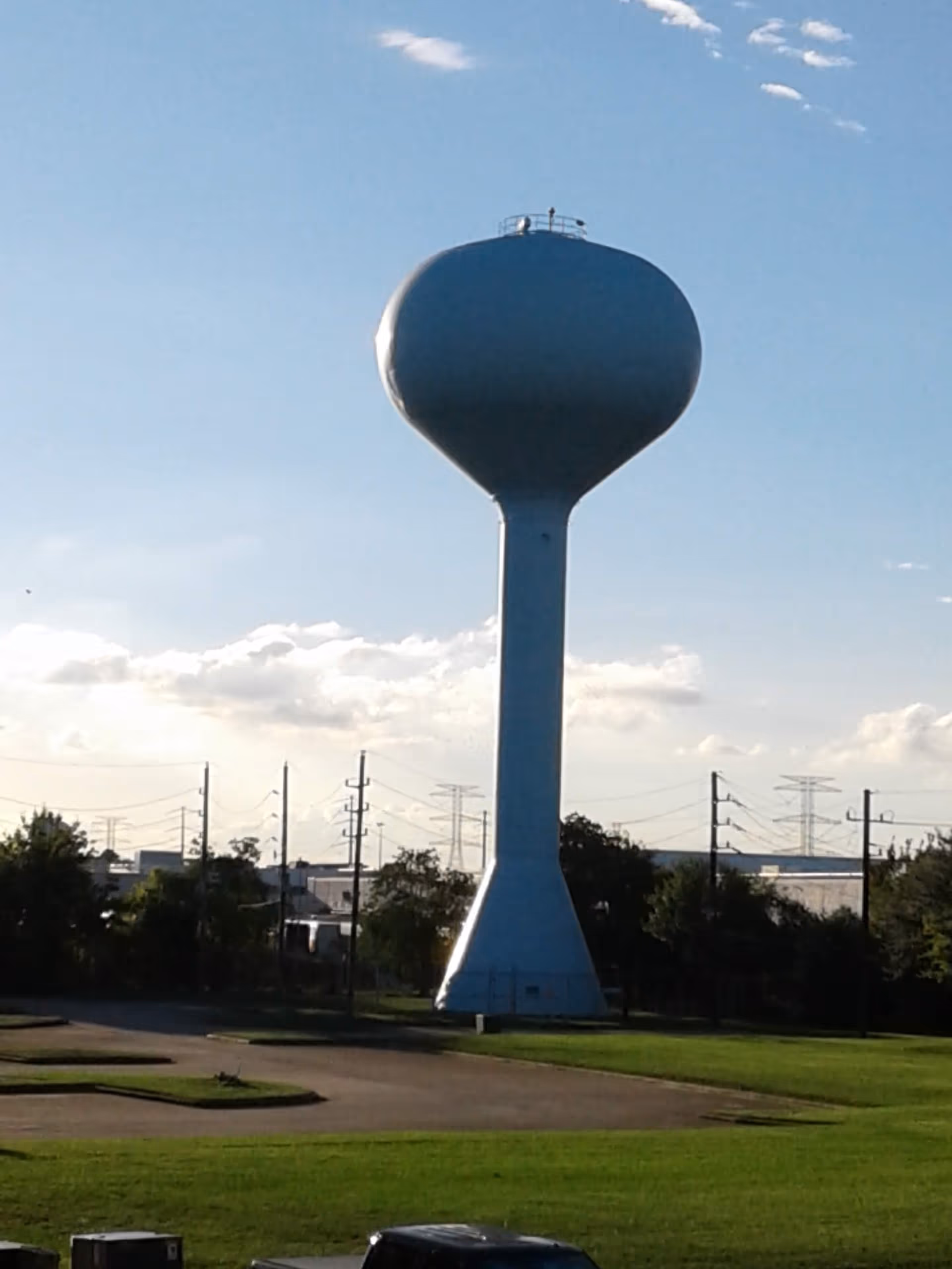 A large blue water tower rises behind a parking lot under a clear sky.