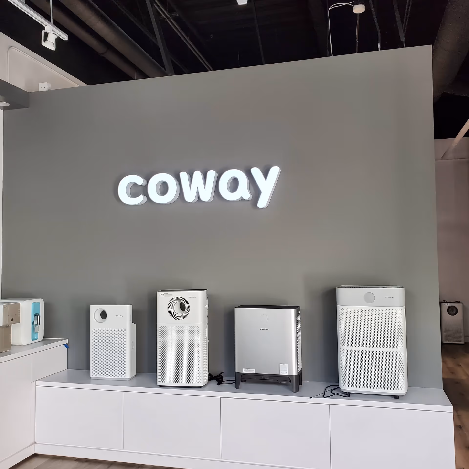 Interior showroom wall with illuminated 'coway' sign and row of air purifiers.