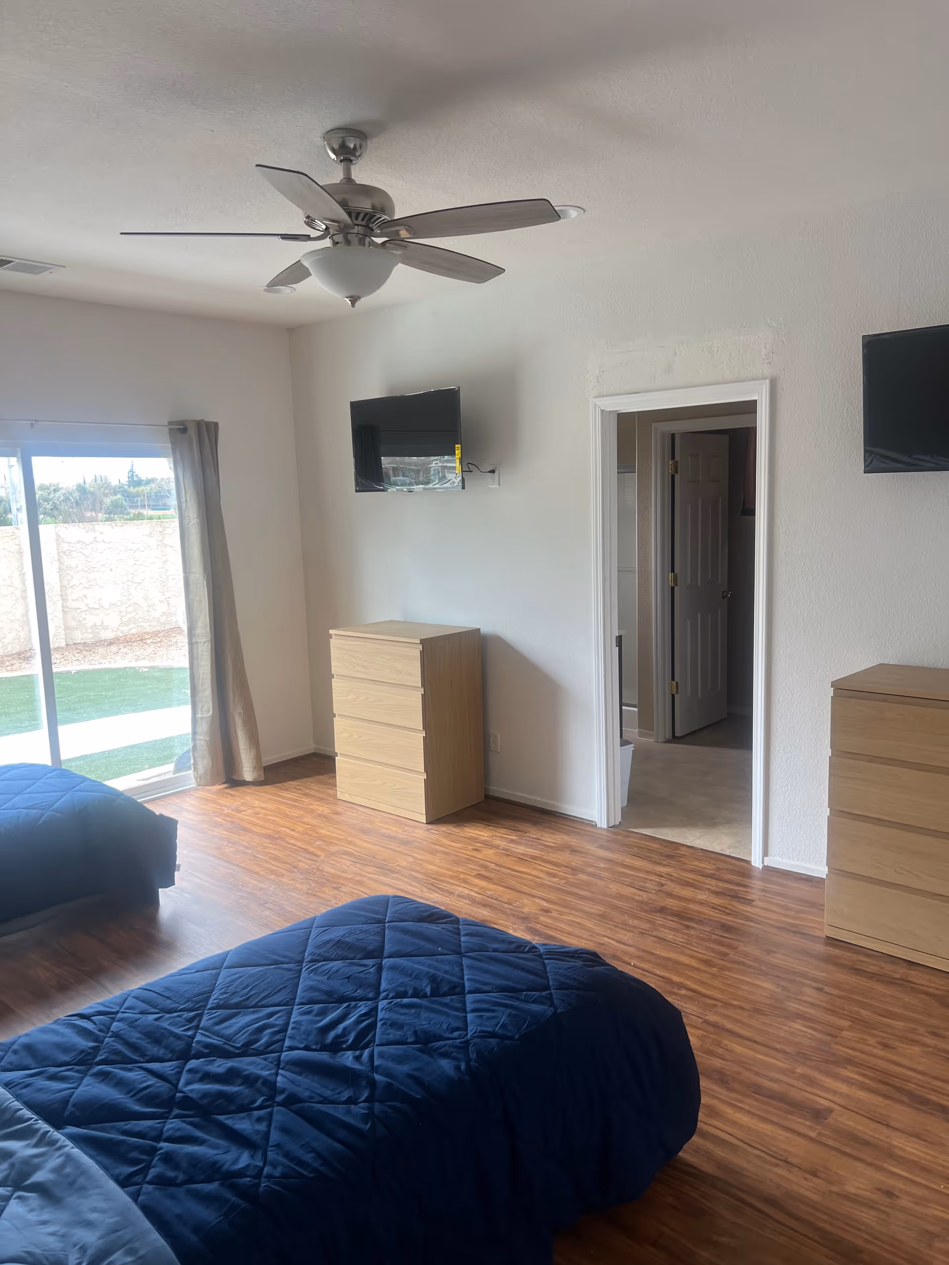 Two single beds with blue quilts, dressers, and a ceiling fan in a senior living bedroom.