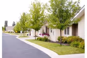 A row of single-story beige assisted living units with green lawns and trees.