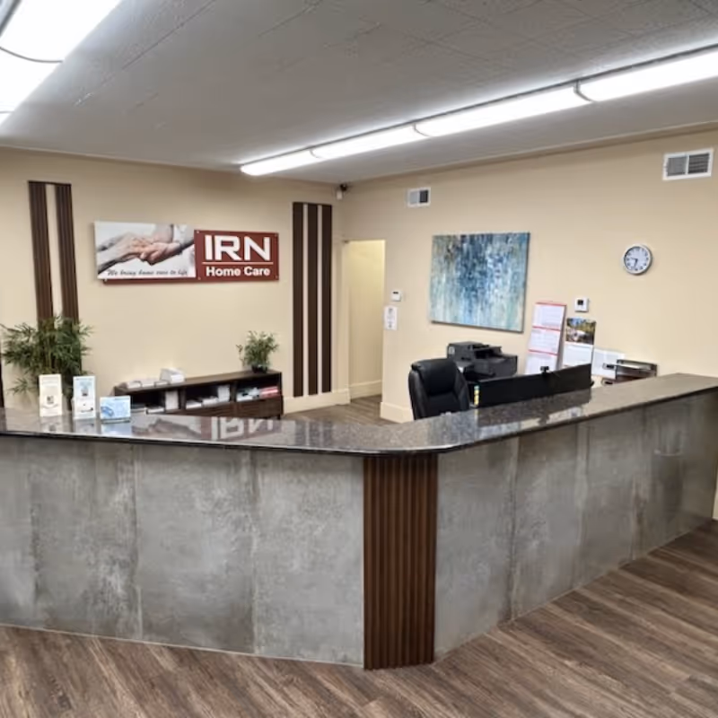 Lobby reception area with curved granite counter, IRN Home Care sign, plants, and wall art.