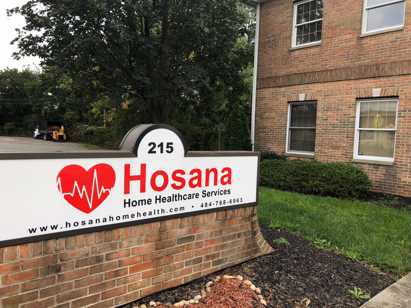 Brick building exterior with a large Hosana Home Healthcare Services sign in the foreground.