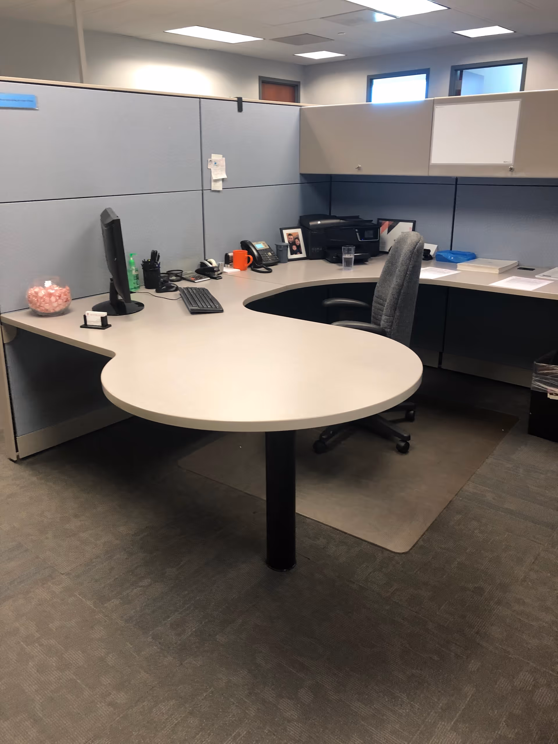 Curved desk with computer and office supplies inside a cubicle workspace.