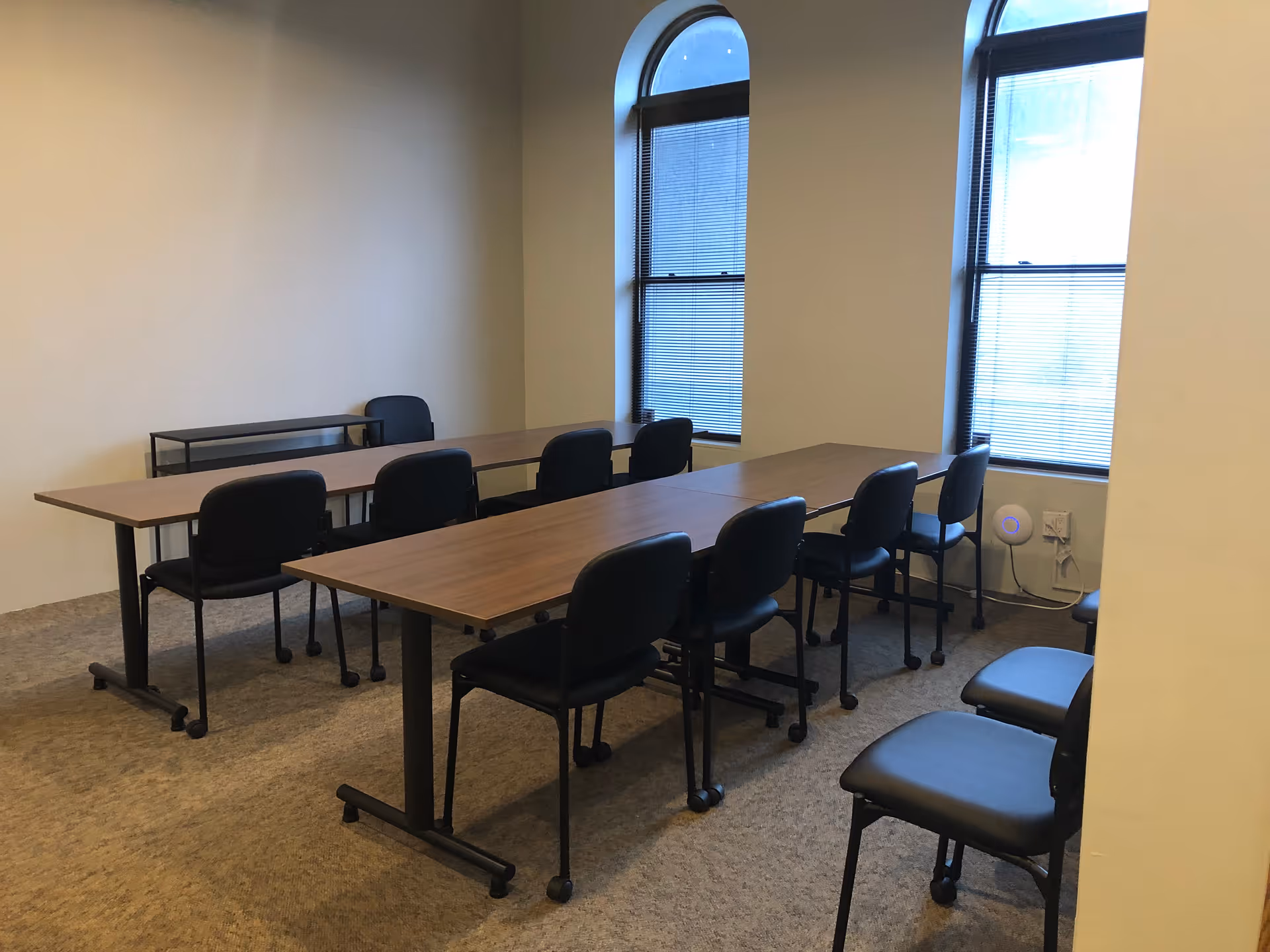 Interior room with long tables, black chairs, and arched windows.