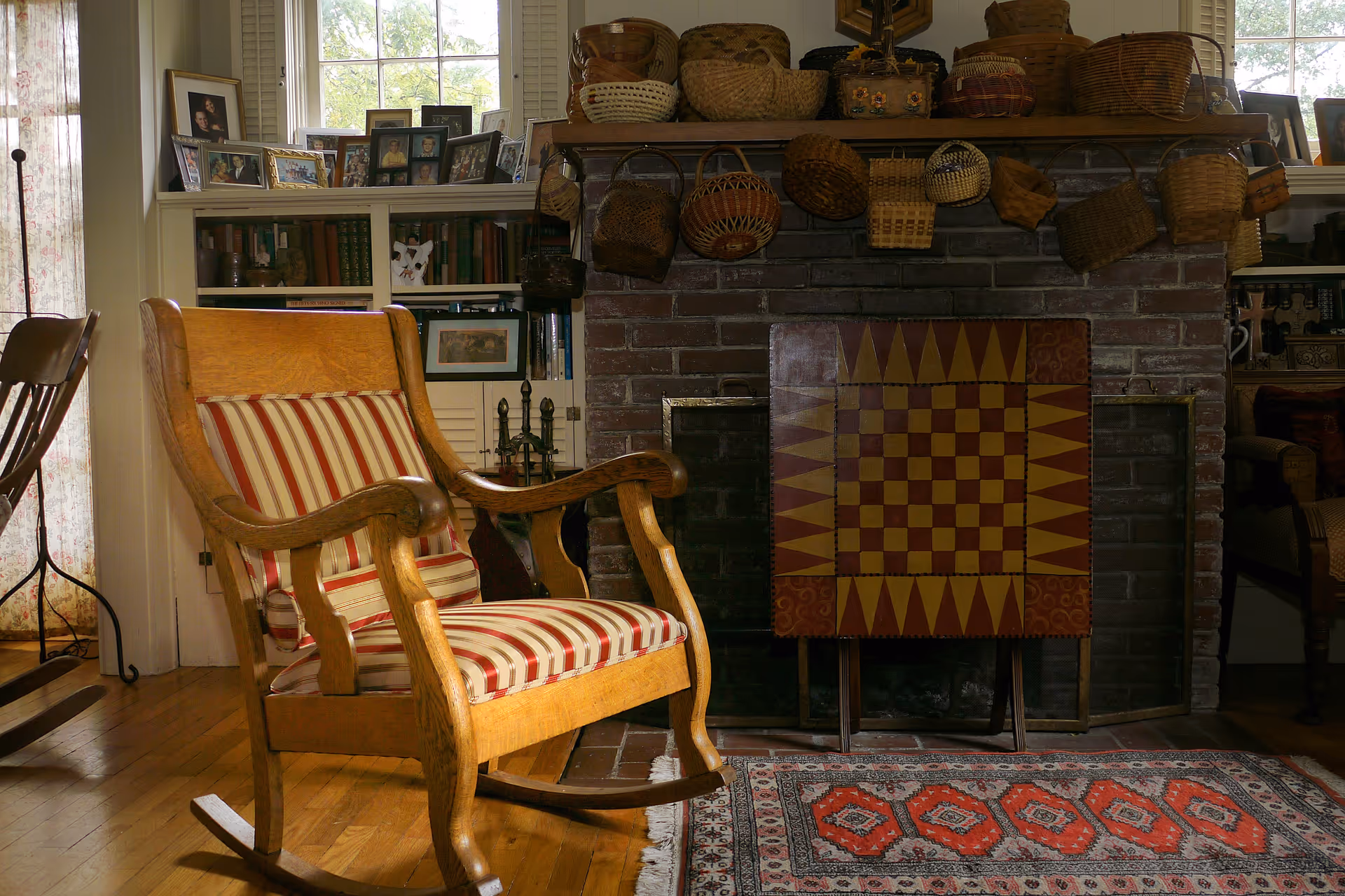 Cozy living room scene with striped upholstered rocking chair, fireplace, baskets, and photos.