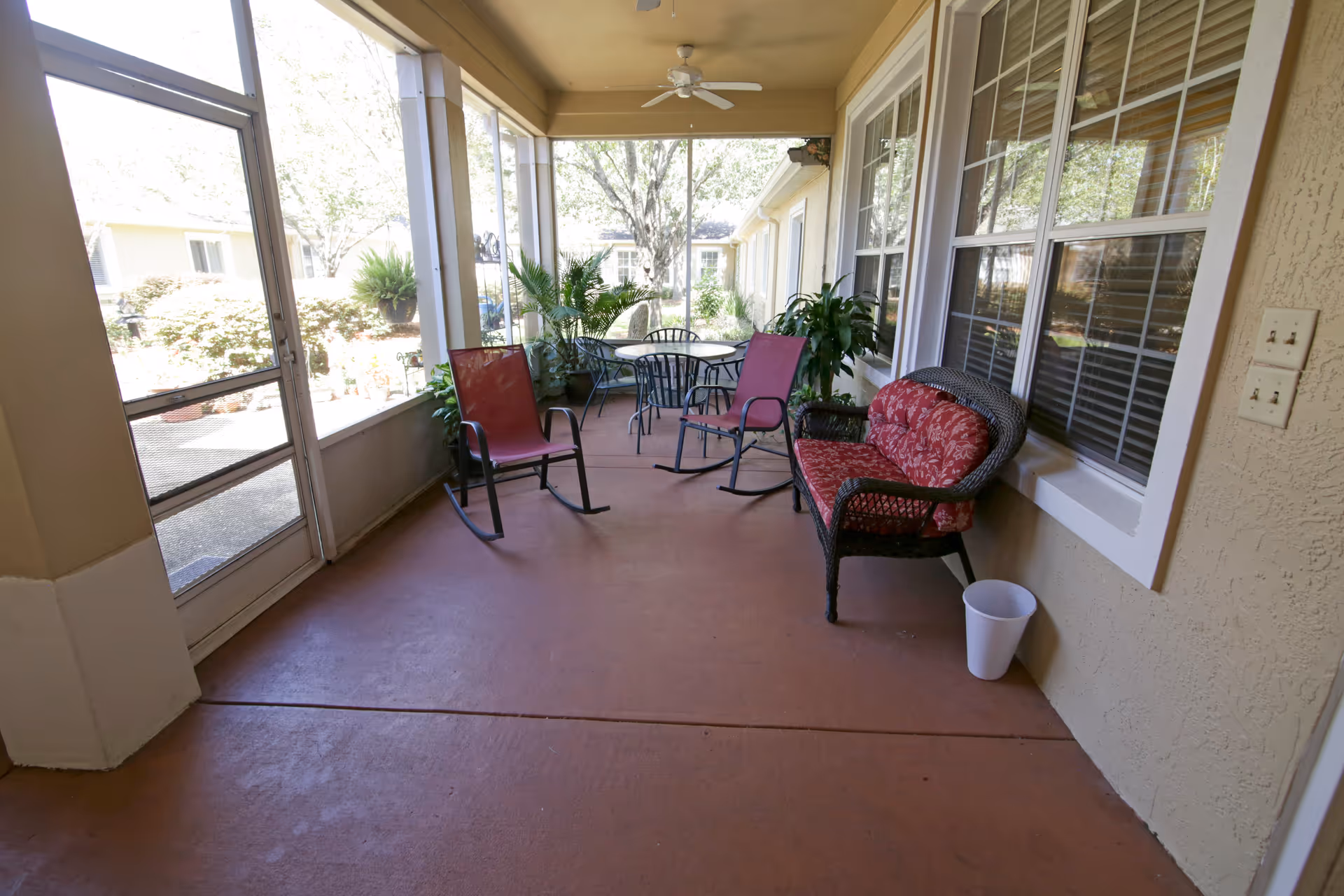 Covered outdoor patio with chairs, a table, potted plants, and a ceiling fan.