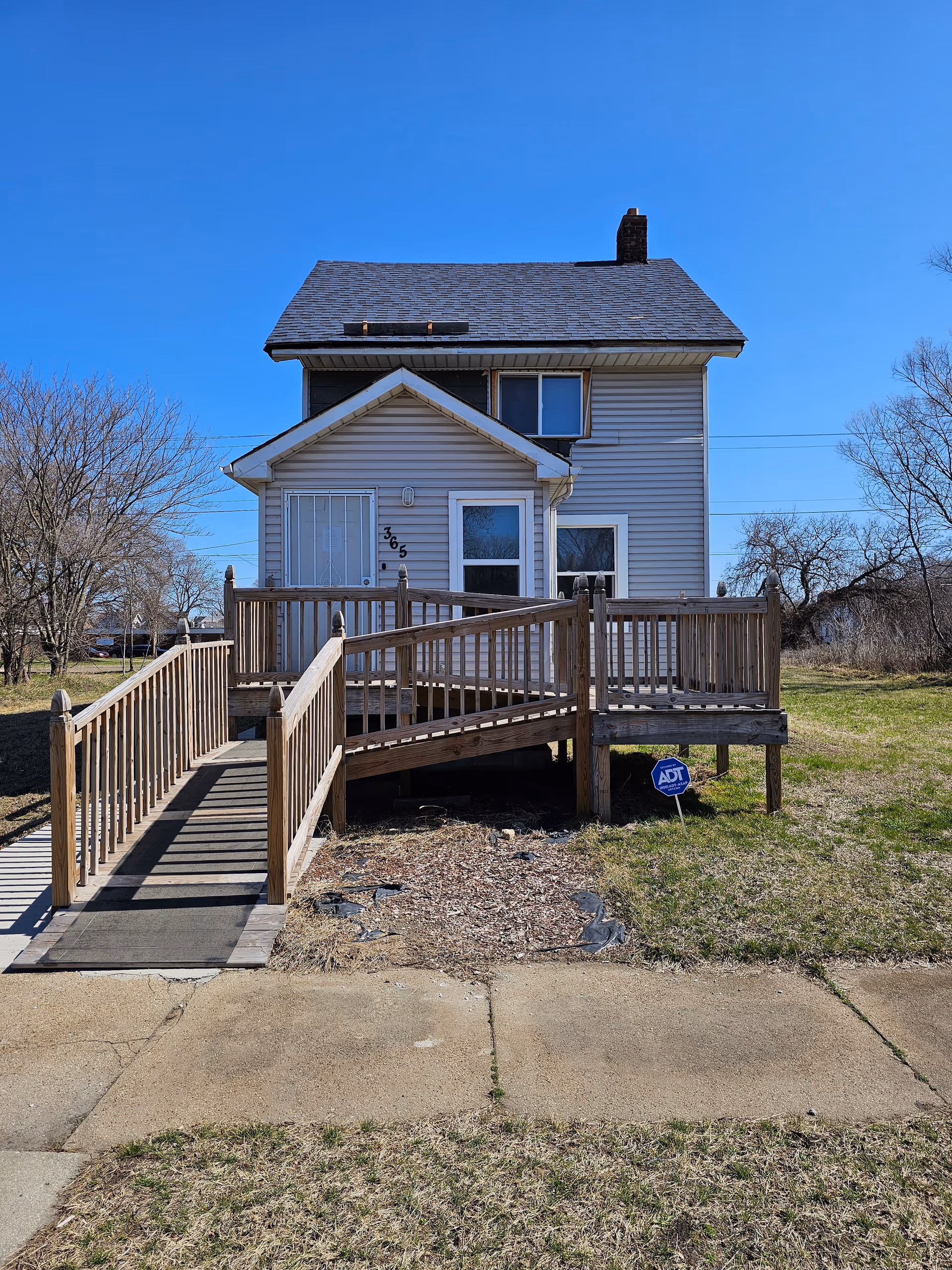 Wood ramp leads to a small two-story house with siding and a peaked front entry.