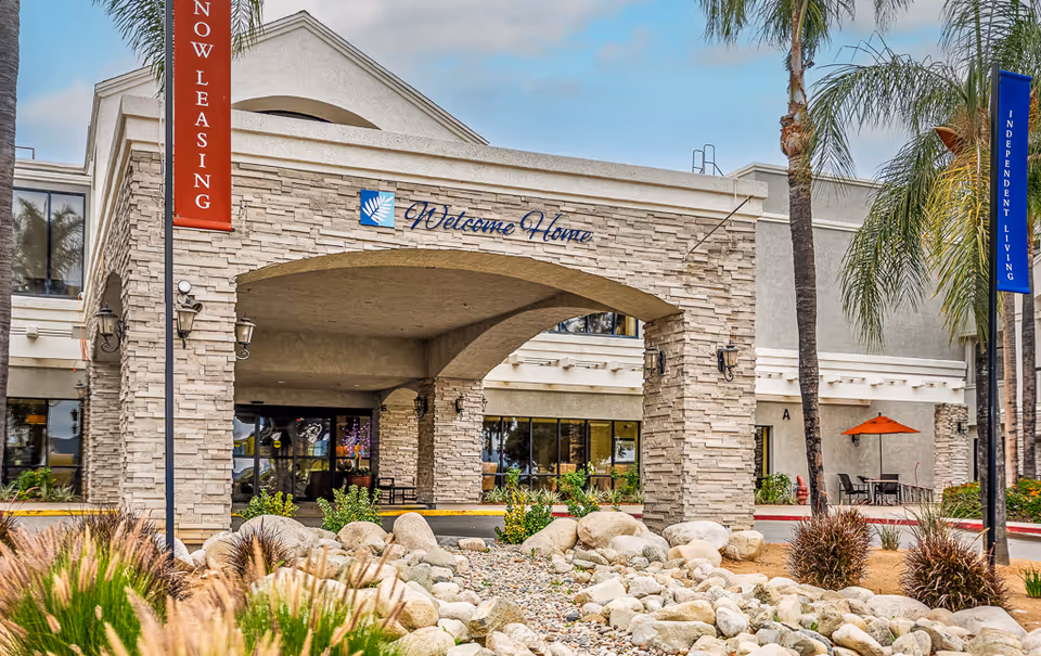 Exterior view of Open Arms senior living entrance with stone arch and outdoor seating.