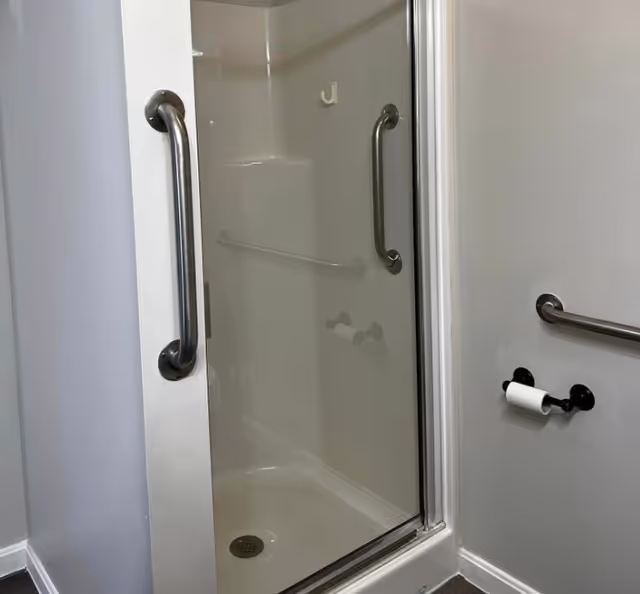 White bathroom with a glass shower door, chrome grab bars, and a towel bar.
